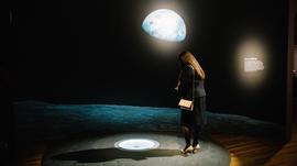 A woman looking down at the floor with an image of the earth on the wall behind her.